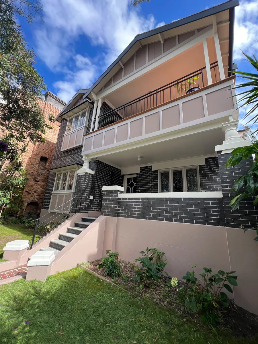 A two storey brick house with rendered panels in soft pink and cream columns, balustrade and trims